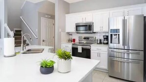 Una cocina moderna con armarios blancos, electrodomésticos de acero inoxidable y una isla central con plantas en macetas.