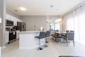 A modern kitchen with stainless steel appliances, a central island with bar stools, and a dining area with a table and chairs.