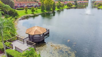 Une vue sur le lac, avec un quai en bois et un belvédère, le tout entouré de verdure et de bâtiments résidentiels.