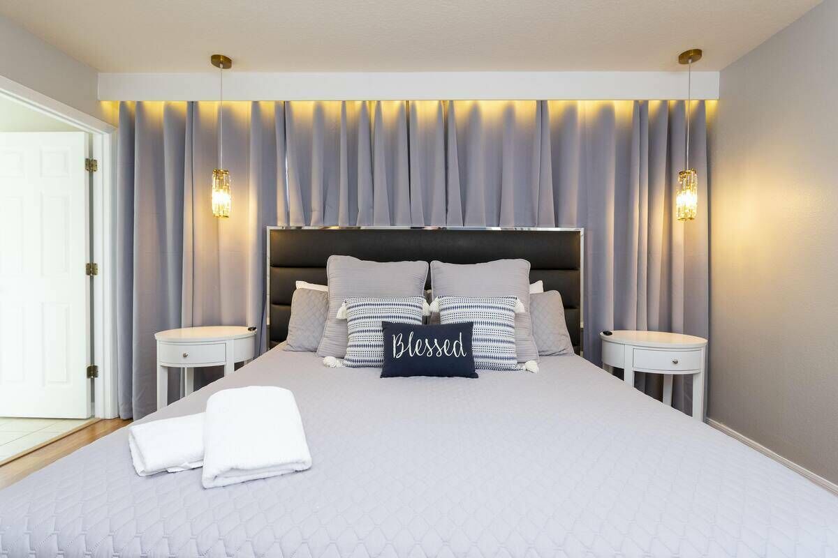 Un dormitorio moderno con una cama grande, dos mesitas de noche y un cabecero con cortinas.