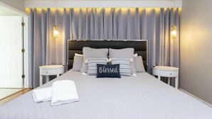 Un dormitorio moderno con una cama grande, dos mesitas de noche y un cabecero con cortinas.