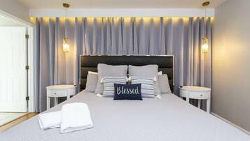 Un dormitorio moderno con una cama grande, dos mesitas de noche y un cabecero con cortinas.
