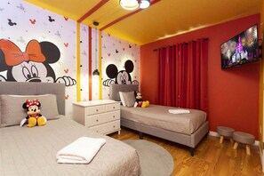 A hotel room with two beds, a TV on the wall, and Mickey Mouse-themed decorations.