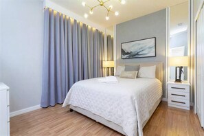 A modern hotel room with a large bed, a bedside table, a lamp, and a painting on the wall.