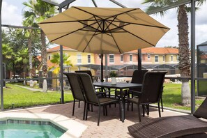 An outdoor patio with a table, chairs, and a pool. - 4BR Pool Home Near Disney at Encantada (Kissimmee)