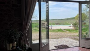 A room with a large glass door leading to an outdoor area with a view of a field and a green structure.