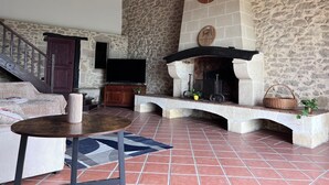A stone-walled living room with a fireplace, a television, and a staircase.