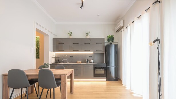 Una cocina moderna con armarios grises, una mesa de comedor de madera y sillas. Hay un refrigerador, un horno y un lavaplatos.