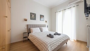 Un dormitorio con cama, mesita de noche, televisor montado en la pared y ventana con cortinas.
