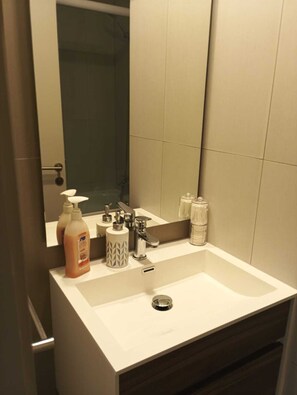 A modern bathroom with a white sink, a mirror, and toiletries. - Urbano Ñuñoa (Santiago)