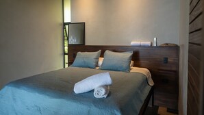 Un lit bien fait, avec une couvre-lit bleue et des oreillers, une tête de lit en bois et un téléviseur fixé au mur.