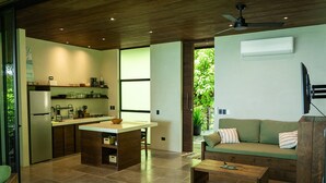 A modern kitchen with a central island, a dining area with a wooden table, and a green sofa with a TV mounted on the wall. - Incredible house with sea view in Santa Teresa (Saint Teresa)