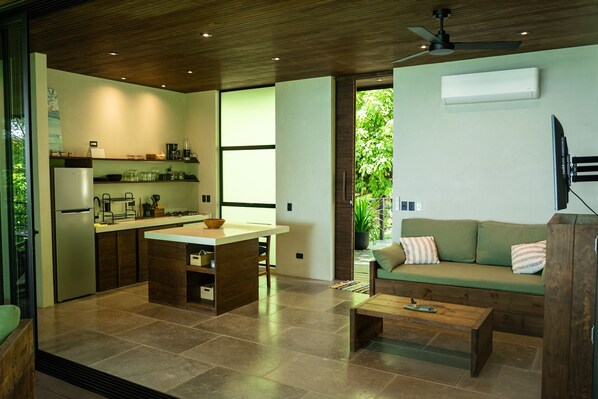 A modern kitchen with a central island, a dining area with a wooden table, and a green sofa with a TV mounted on the wall. - Incredible house with sea view in Santa Teresa (Saint Teresa)