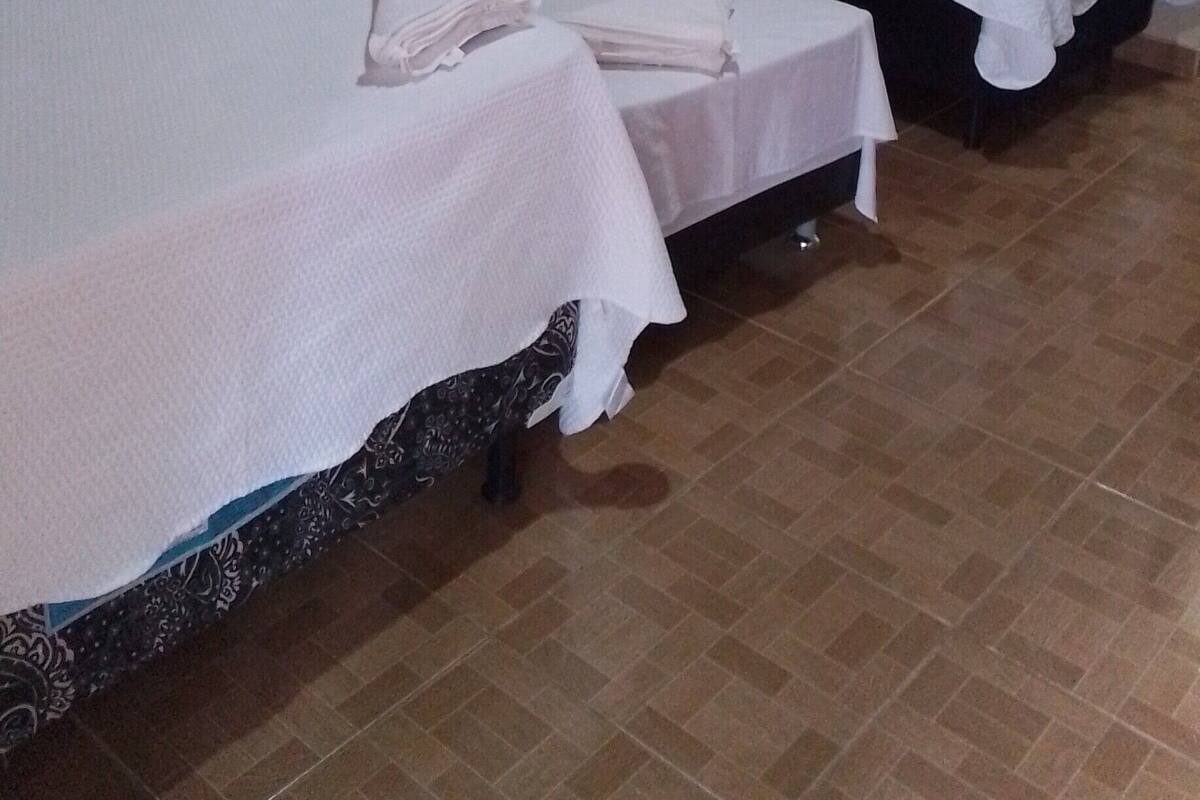 Une chambre d’hôtel avec deux lits, chacun recouvert de draps blancs, une petite table sur laquelle est pliée une serviette, et un tableau accroché au mur.