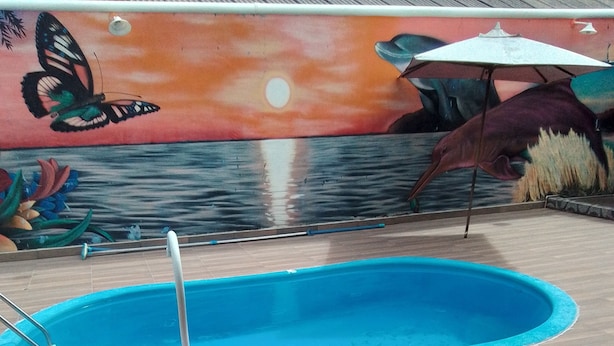 A swimming pool with a wooden deck and a mural in the background. - Pousada Sossego Ronaldo e Clarinha  (Santarem)