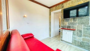 A living room with a red sofa, a stone wall, a flat-screen TV, and a wooden ceiling. - Appartamento Oasi - Affitti Brevi Italia (Bardonecchia)