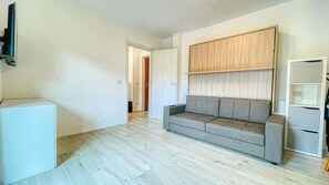 A room with a grey sofa, a white cabinet, and a wooden panel wall. - Appartamento Oasi - Affitti Brevi Italia (Bardonecchia)
