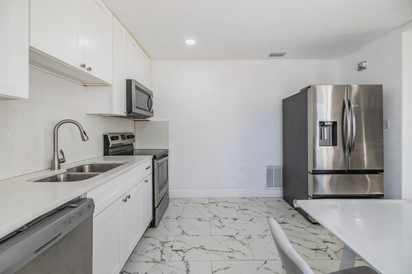 A compact kitchen with white cabinets, a stainless steel refrigerator, a microwave, a sink, and a dishwasher.