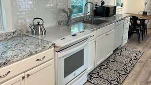 Una cocina moderna con armarios blancos, una campana extractora de acero inoxidable, horno integrado, encimera de granito y alfombra con estampado blanco y negro.