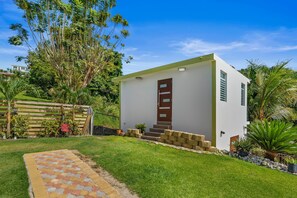 Une maison moderne de plain-pied, avec une façade blanche, une porte marron et un petit porche à l’avant.