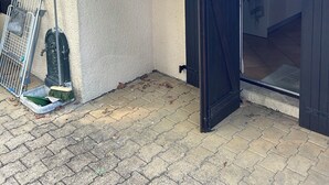 Un patio con suelo de baldosas, una reja de metal, una escoba y un dispensador de agua.