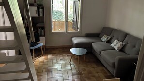 Una sala de estar con suelo de espiga, un sofá gris con cojines estampados, una mesita redonda y una estantería.