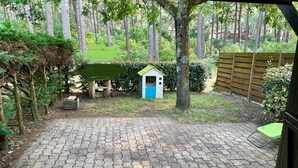 Un patio empedrado con un cobertizo pequeño, una valla de madera y un árbol.
