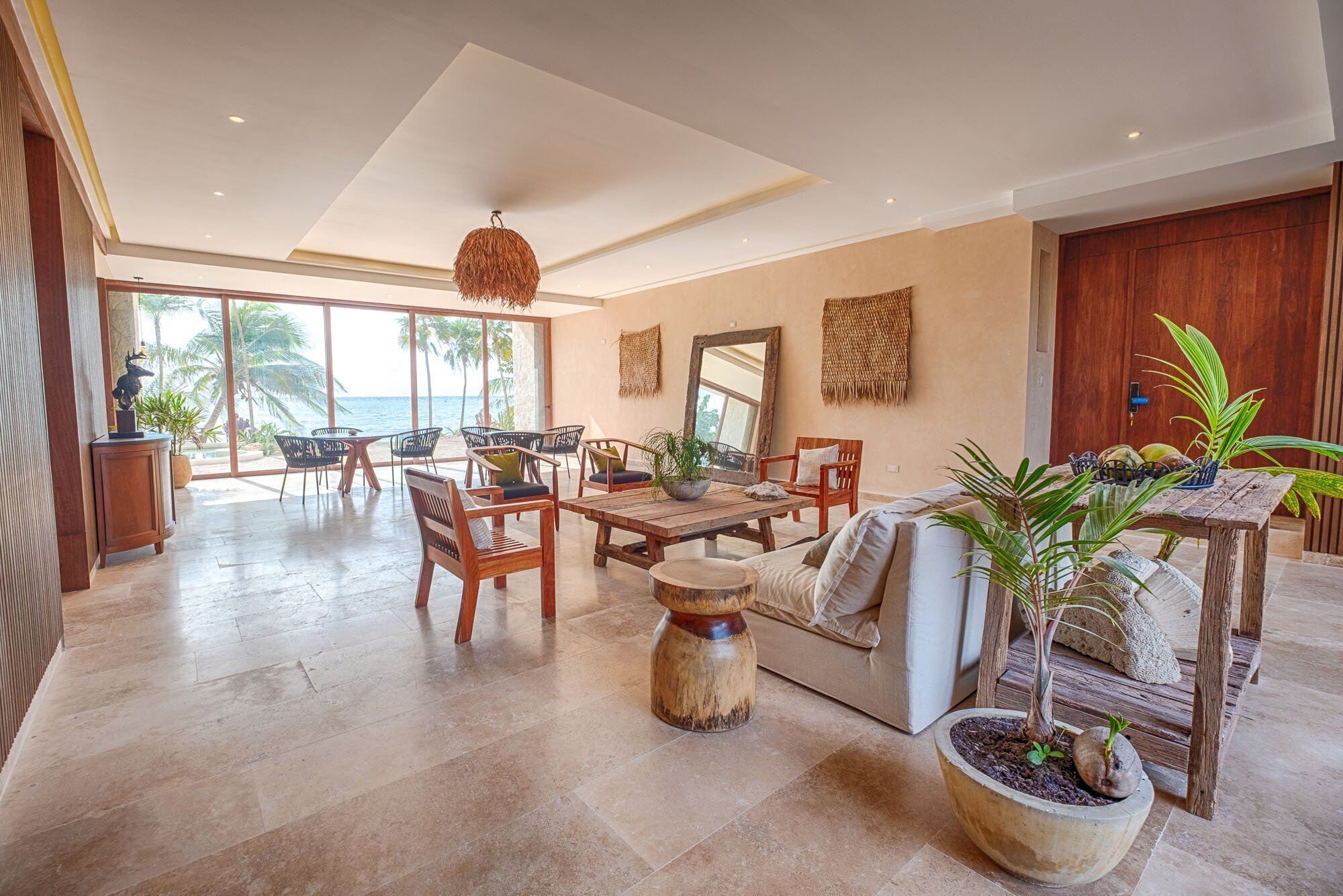 Ruime woonkamer met groot raam met uitzicht op een strand, ingericht met houten meubels en een centrale salontafel.