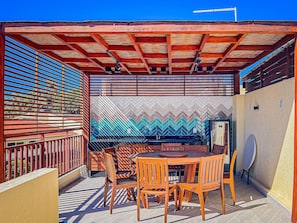 An outdoor patio with a wooden table and chairs, a patterned wall, and a metal grill. - Solar Água Pipa (Tibau do Sul)