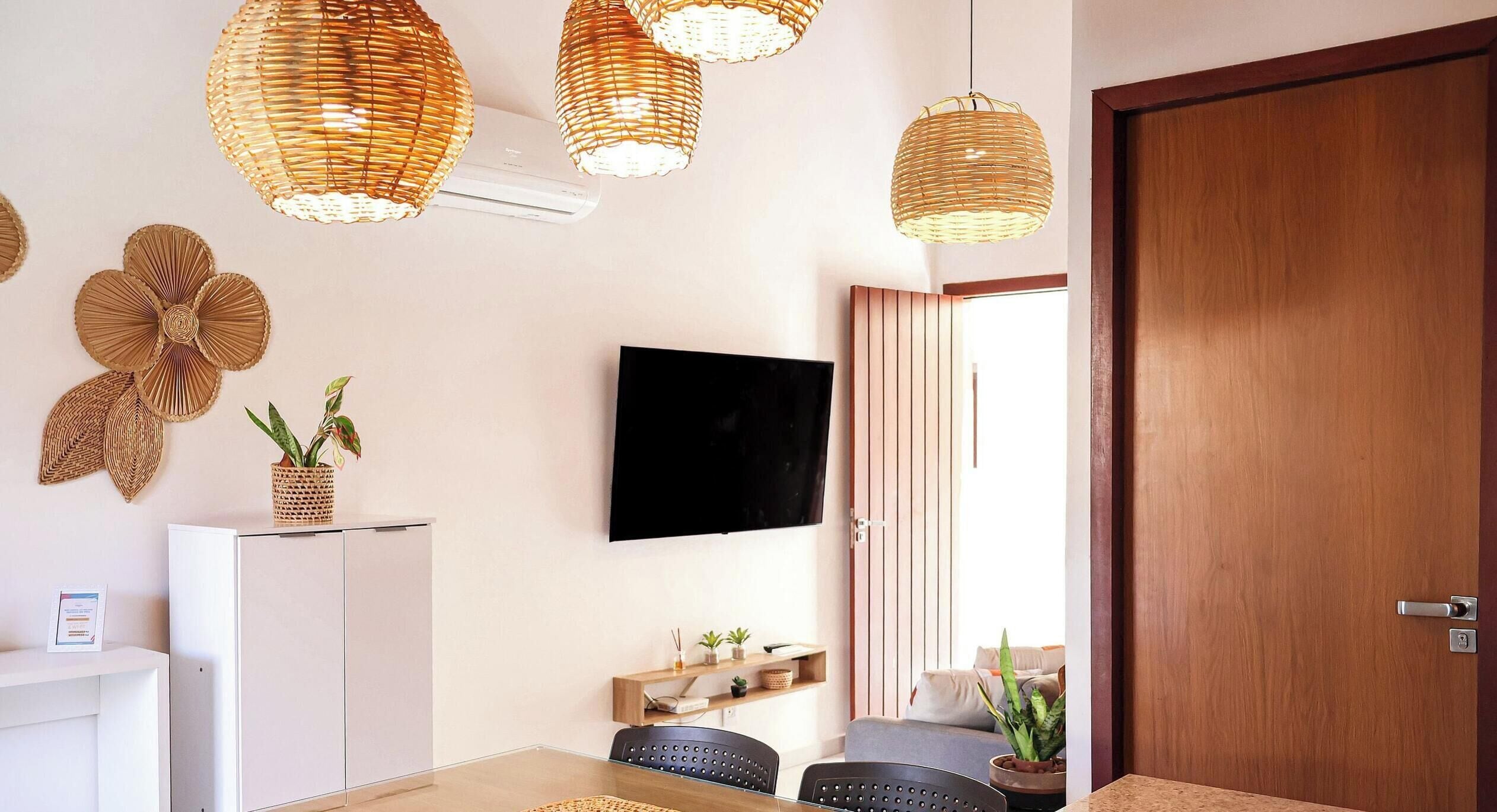 Una sala de estar moderna con un televisor de pantalla plana, lámparas de techo de mimbre, una puerta de madera y una mesa de recepción.