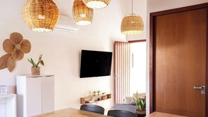 Una sala moderna con televisor de pantalla plana, lámparas colgantes de mimbre, una puerta de madera y un comedor con mesa y sillas.