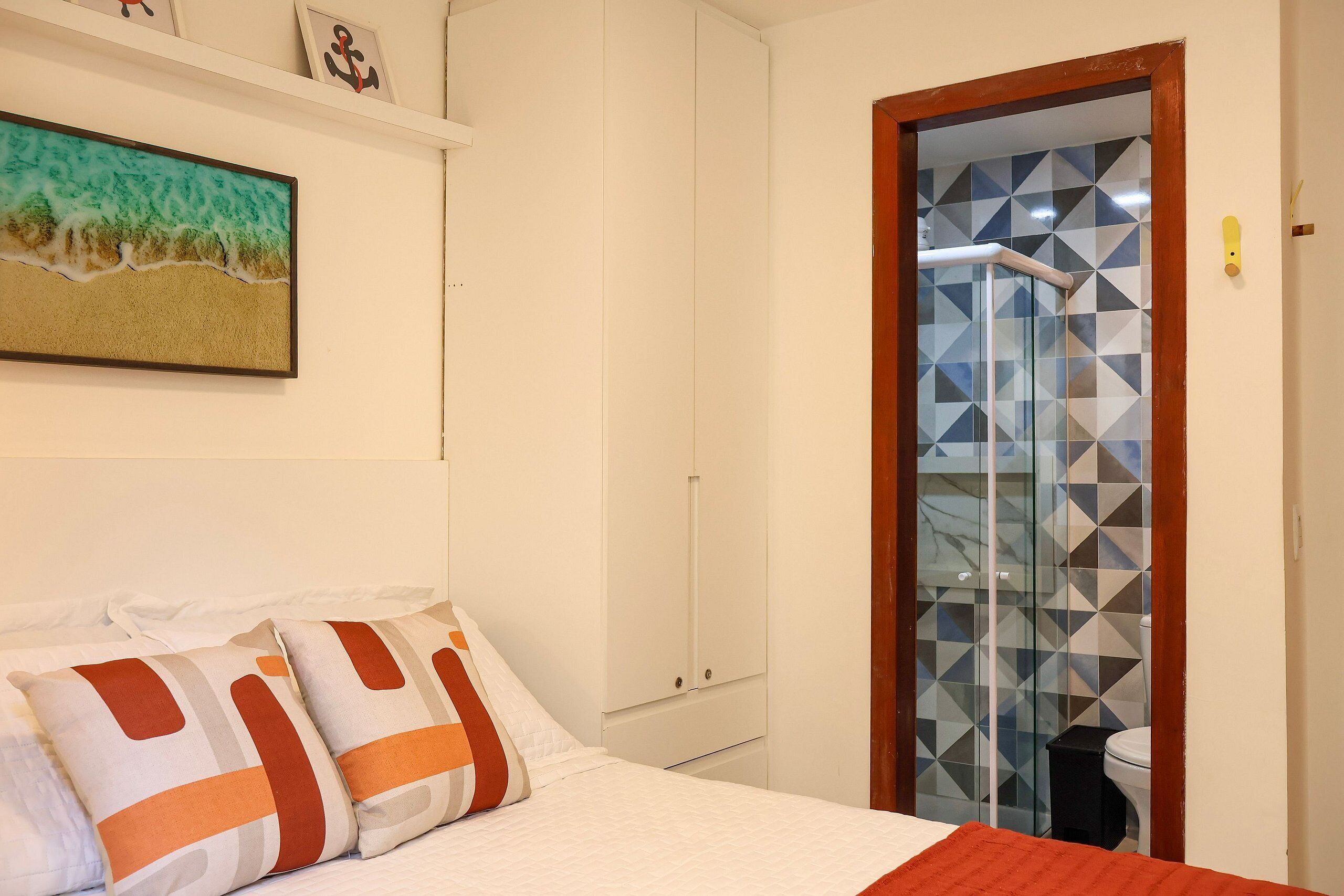 A bedroom with a bed, pillows, a wardrobe, and a shower with geometric tiles.