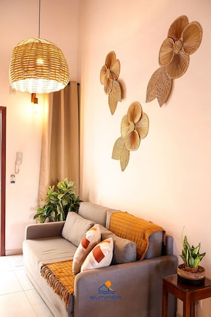 Un salon moderne avec un canapé, un luminaire suspendu, des œuvres d’art mural et une petite table sur laquelle est posée une plante.