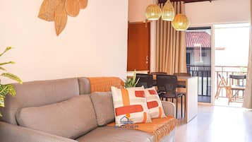 A living room with a sofa, a dining area with chairs, a table, and a balcony with a view.