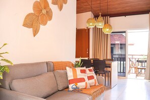 A living room with a sofa, a dining area with chairs, a table, and a balcony with a view. - Solar Água Pipa (Tibau do Sul)