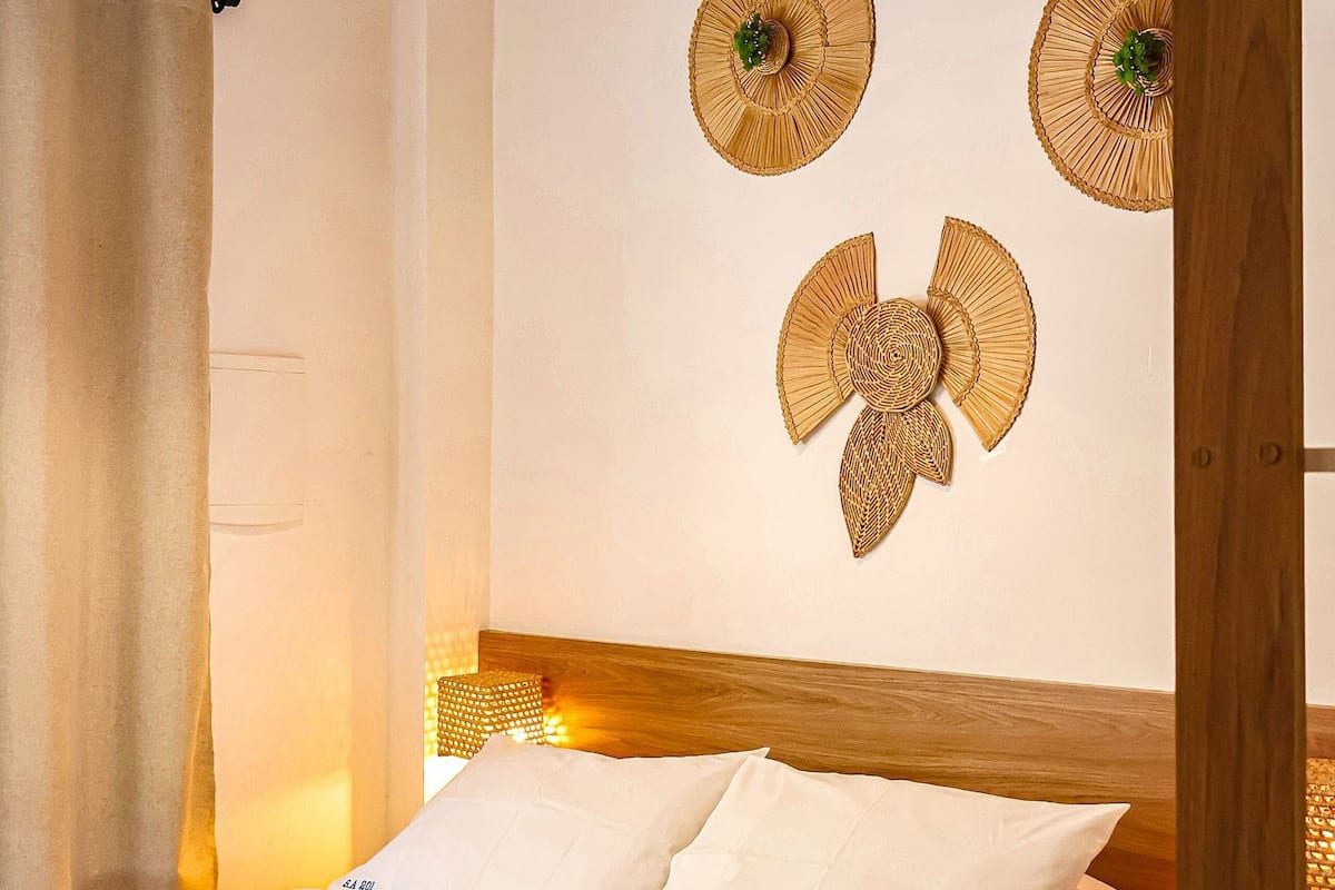 A neatly made bed with white bedding, a woven wall hanging, and a ceiling light fixture.