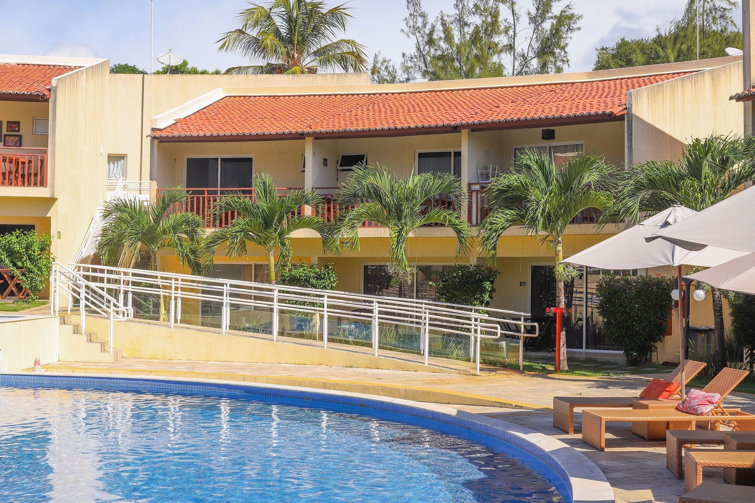 Un hôtel doté d’une piscine, d’un espace extérieur aménagé et d’un toit recouvert de tuiles rouges.