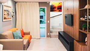 Una sala de estar moderna con un sofá, televisión y una escalera que lleva a un espacio al aire libre.