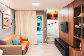 Un salon moderne avec un canapé, un téléviseur et un escalier menant à un espace extérieur.