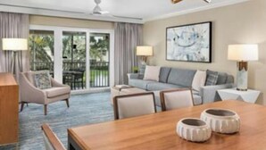 Habitación de hotel con zona de comedor, sofá y balcón con cortinas.