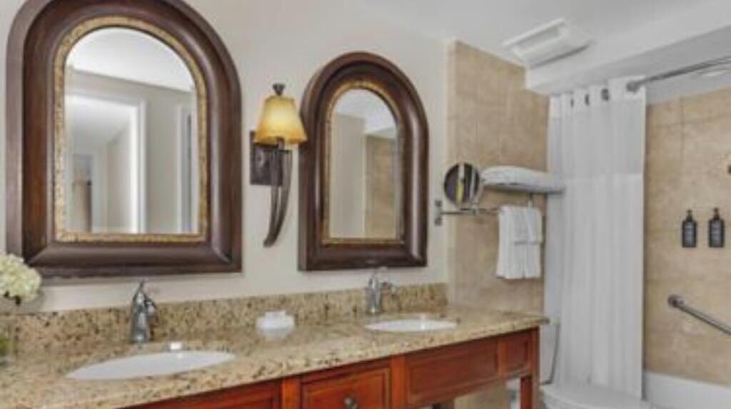 A bathroom with two sinks, a large mirror, a shower, and a towel rack.