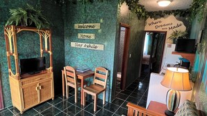 A cozy room with a TV on a wooden cabinet, a small table with chairs, and a sofa. - RAINFOREST ROOM - Close to Beach - One Bedroom Suite (San Pedro)