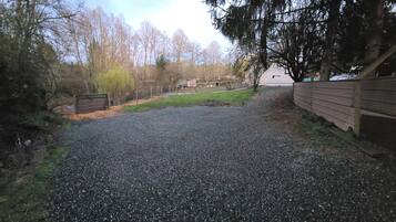 Een grindpad leidt naar een houten poort, omringd door bomen en een gazon.