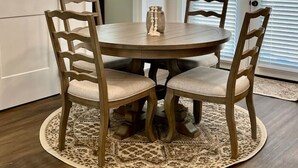 A dining area with a round wooden table, four wooden chairs, and a decorative vase.