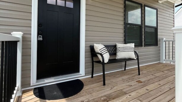 A porch with a black door, a bench with cushions, and a white railing.