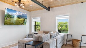 A modern living room with a sofa, a coffee table, two windows, and a painting on the wall. - Johnsons Cove - Lakefront Retreat With EV Charger (Seneca)