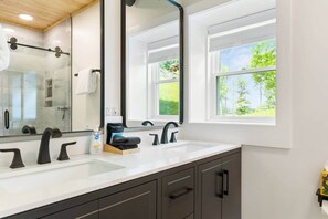 Ein modernes Badezimmer mit einem großen Spiegel, zwei Waschbecken und einem Fenster mit Blick ins Grüne.
