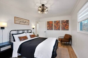 Ein Schlafzimmer mit einem Bett, einem Sessel, einem Wandbild und einer Deckenleuchte.