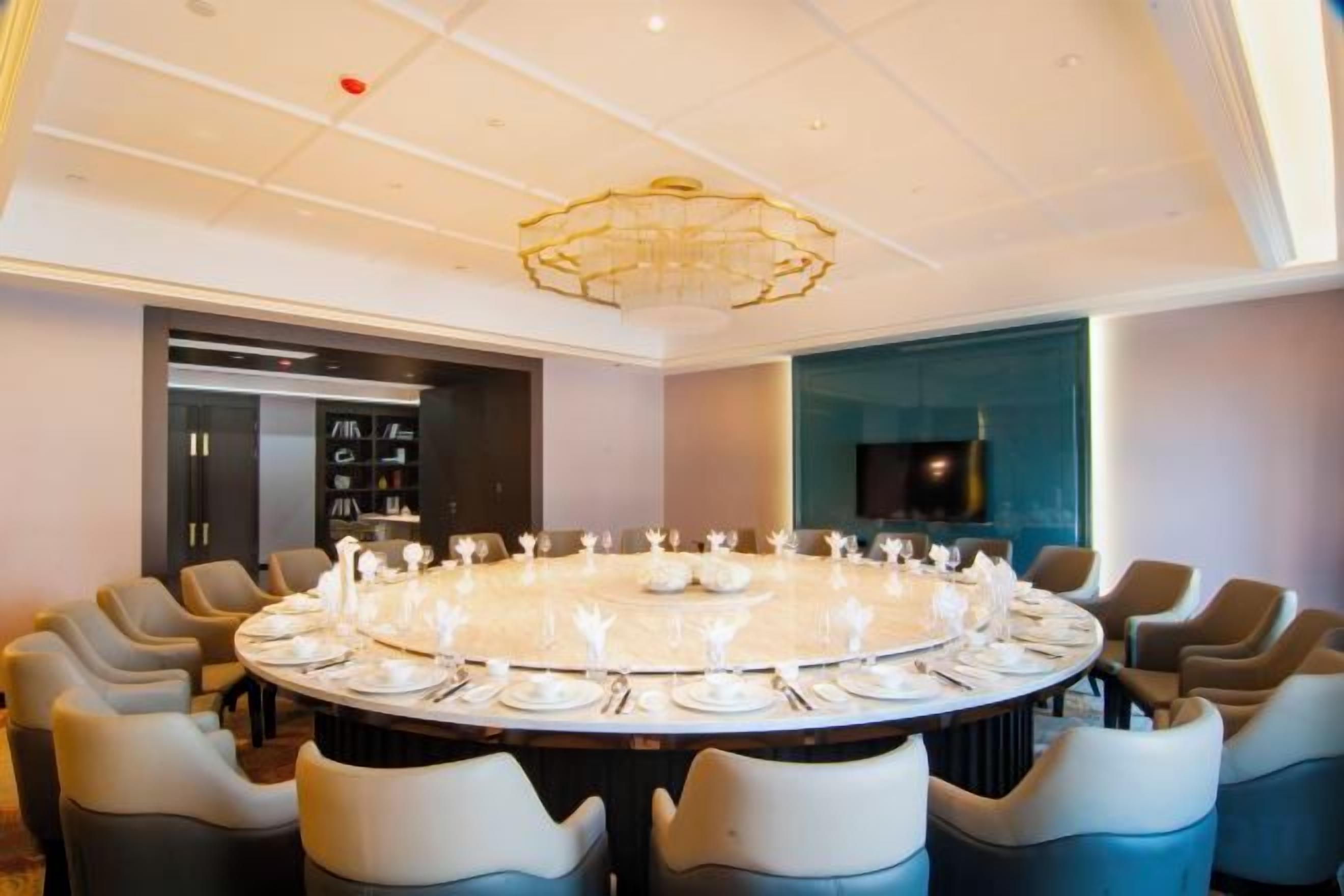 A round table set for dining with chairs around it, a chandelier above, and a television on the wall.