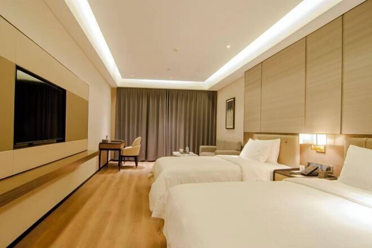 A hotel room with two beds, a TV, a desk, a chair, and a curtain.